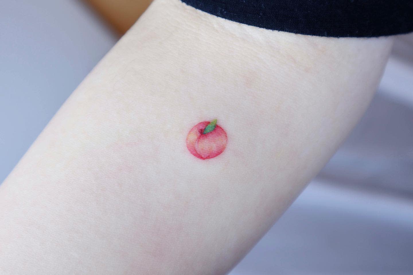 Small peach tattoo with a green leaf on an inner forearm